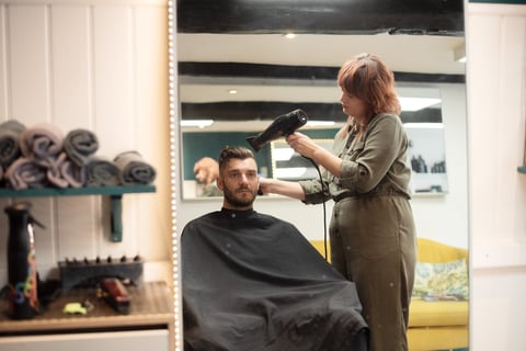 Hairstylist blow-drying a male clients hair in a modern salon with mirrors and styling tools