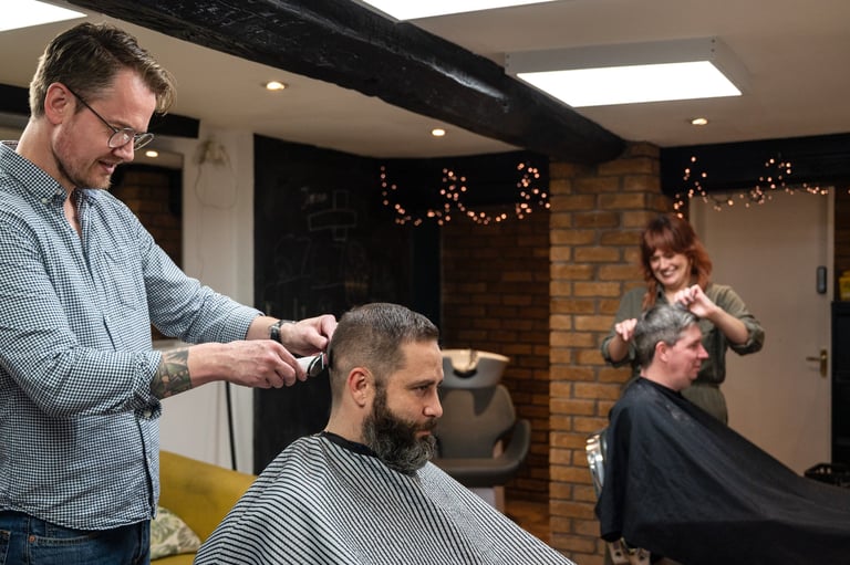 Barber cutting a customers hair in a salon with holiday decorations and a woman watching in the background