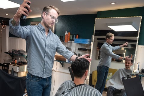Man cutting clients hair in a salon while another stylist works in background